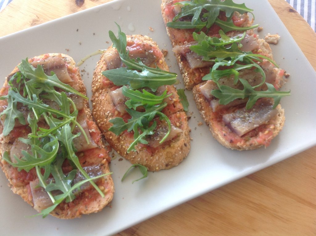 Tosta de sardina ahumada con base de tomate y cubierta de rúcula