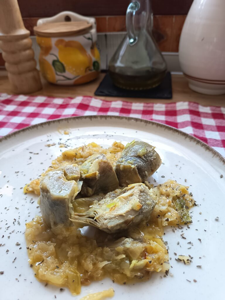 Corazones de alcachofa cocidos con salsa cremosa de puerros y pistachos, servidos como plato saludable y aromático.