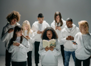 Representación del contraste entre una persona leyendo un libro y un grupo con los smartphone juzgandola con la mirada como si fuera una rara avis