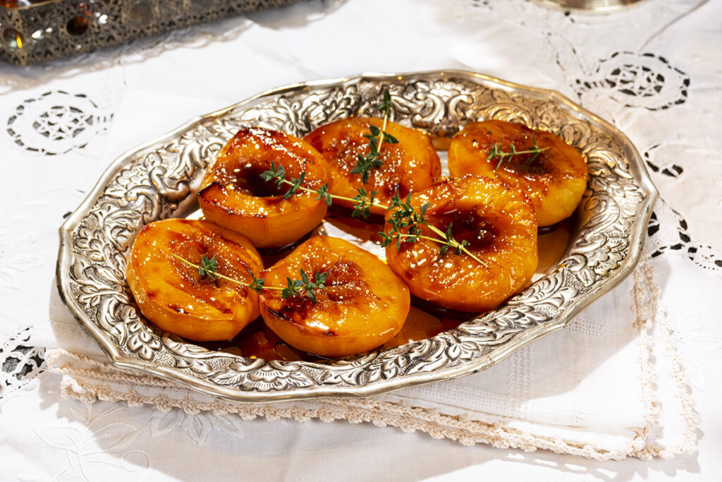Mitades de melocotón flambeados rellenos de mascarpone, con frutos secos picados y fideos de chocolate por encima.